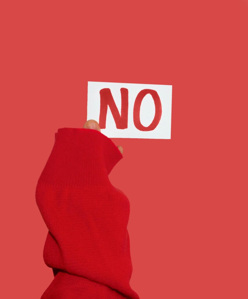 A person in a red sleeve holds a card with 'NO' written on it against a matching red wall.