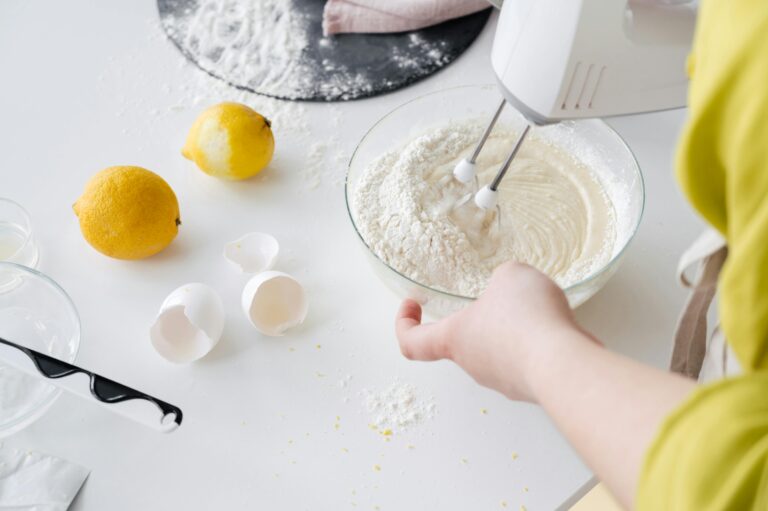 From above of crop anonymous female with mixer preparing cake dough at table with fresh lemons and eggshells in house.veganer zitronenkuchen