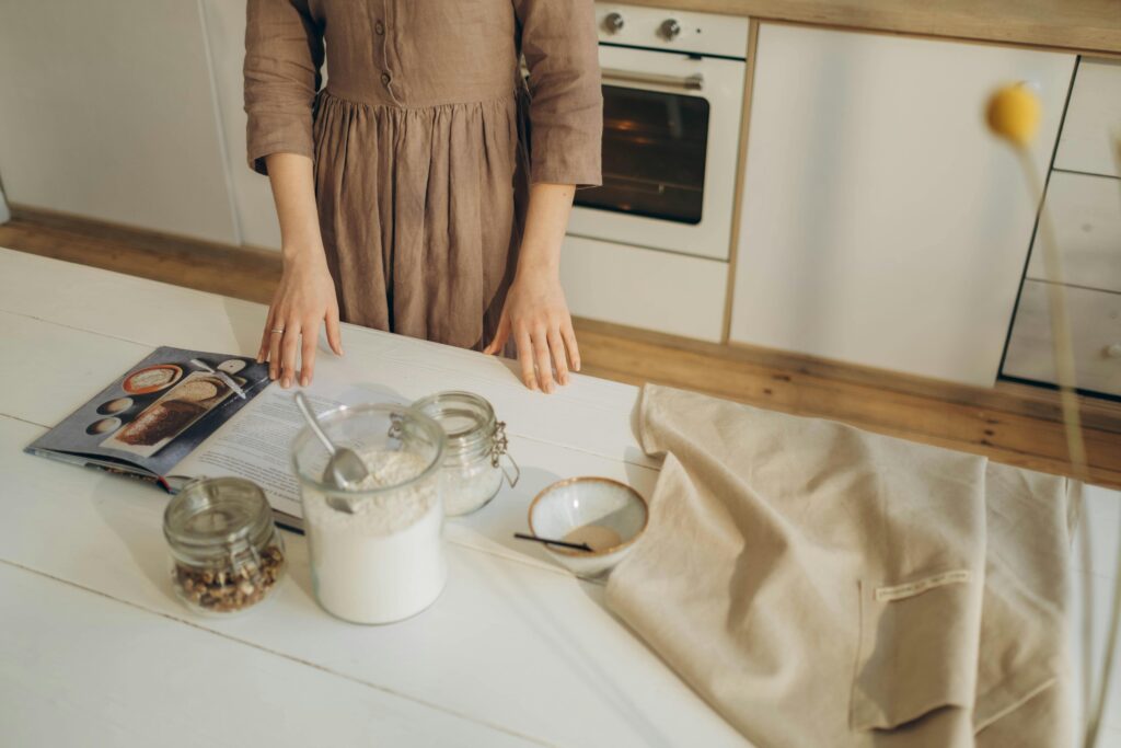 A person prepares ingredients on a wooden kitchen table with a cookbook for baking. veganer zitronenkuchen