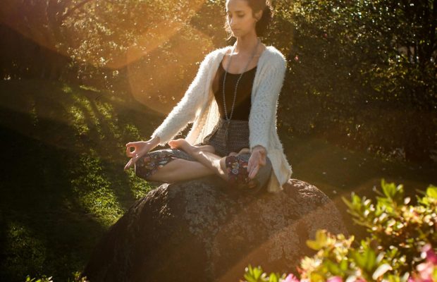 pexels-photo-2597205-2597205 Woman in tranquil meditation pose outdoors, bathed in sunlight, surrounded by lush greenery.